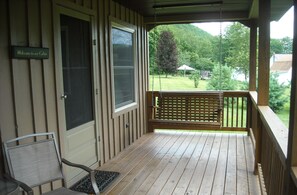 A wooden porch with a bench and a chair, a door with a sign, and a view of a green landscape.