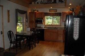 A kitchen with wooden cabinets, a refrigerator with a welcome sign, a dining table with chairs, and a view of the outdoors through the windows.