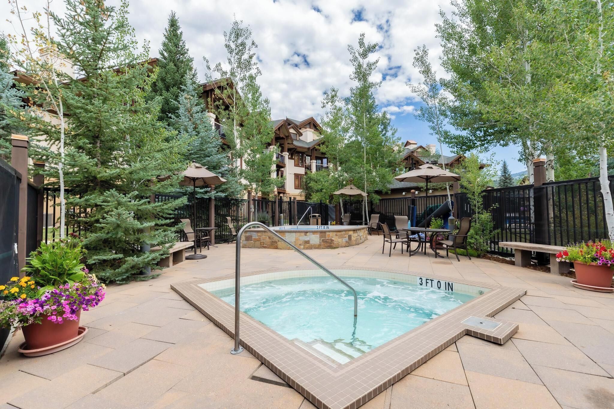 A pool area with a hot tub, surrounded by potted plants and outdoor seating.