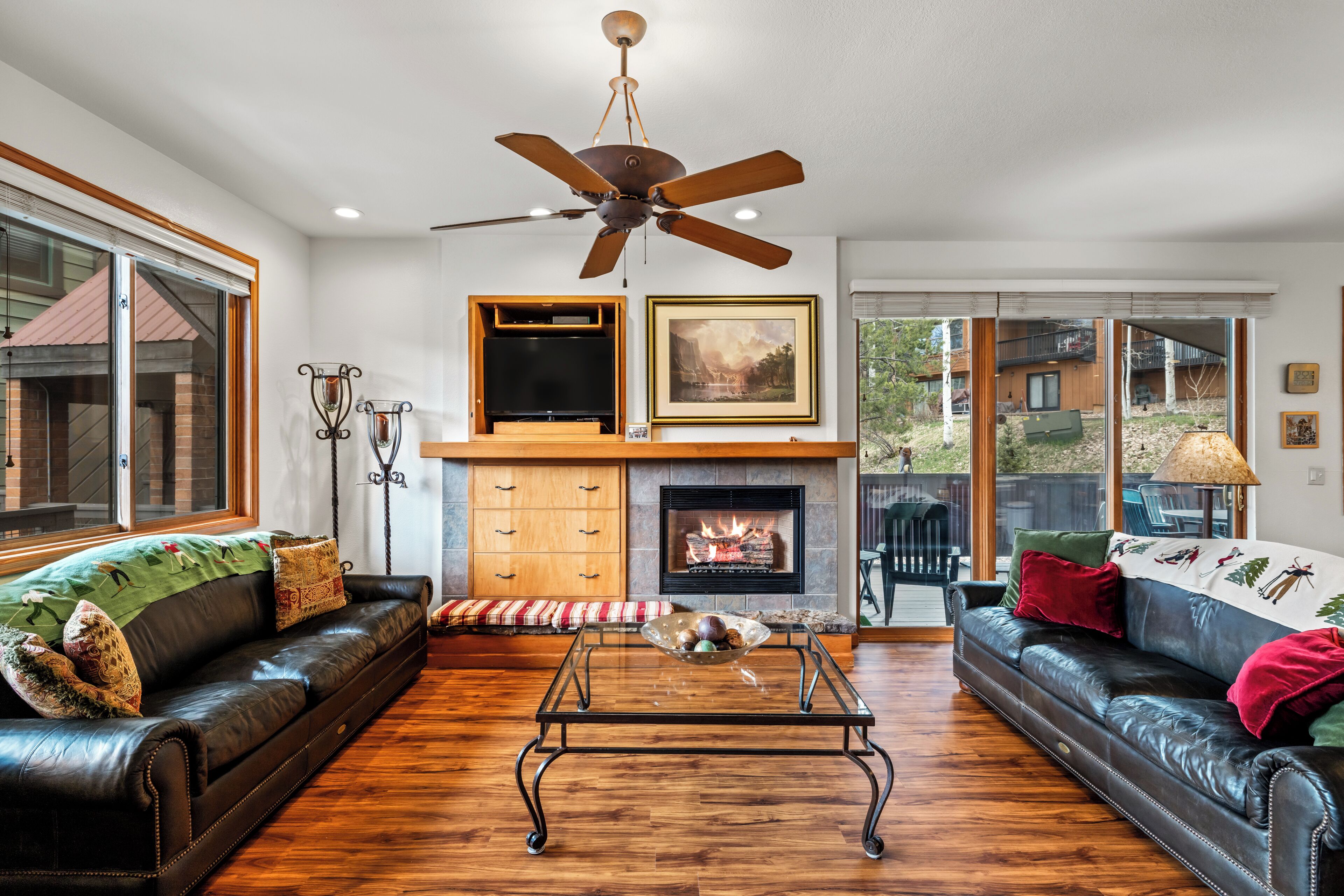 A living room with a fireplace, leather sofas, a coffee table, and a ceiling fan.