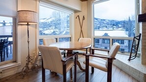 Un coin repas avec une table ronde et quatre chaises, de grandes fenêtres donnant sur un paysage enneigé et une lampe sur le côté gauche.