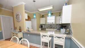 A kitchen with a central island, white bar stools, a wooden dining table, and pendant lights. - 4673 Wild Iris Dr 203 2 Bedroom Condo by Redawning (Myrtle Beach)
