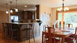 A kitchen with wooden cabinets, a central island with bar stools, a dining table with chairs, and a chandelier. - Flying Monkey Mesa | Near Zion | Rustic Mtn Home (Virgin)