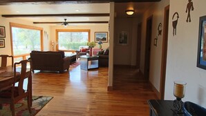 A spacious living area with wooden floors, a dining table with chairs, a sofa, and a coffee table. There is a hallway leading to another room. - Flying Monkey Mesa | Near Zion | Rustic Mtn Home (Virgin)