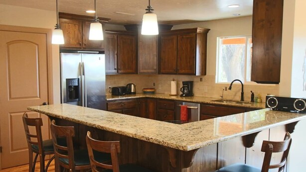 A kitchen with a large island, wooden cabinets, and bar stools. - Flying Monkey Mesa | Near Zion | Rustic Mtn Home (Virgin)