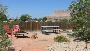 A backyard with a wooden fence, picnic tables, and a red chair. - Flying Monkey Mesa | Near Zion | Rustic Mtn Home (Virgin)