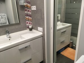 Un baño moderno con un lavamanos blanco, un espejo y un box de ducha de vidrio.