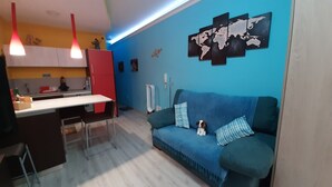 A modern kitchen with a red cabinet, a white countertop, and a blue sofa with two pillows. There is a world map on the wall and a hanging light fixture. - Casa a Medida (Las Palmas de Gran Canaria)