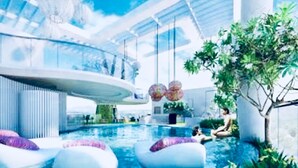 Ein moderner Poolbereich im Innenbereich mit Glasdach, einer zentralen Wasserspende und einer Sitzecke mit Baum.