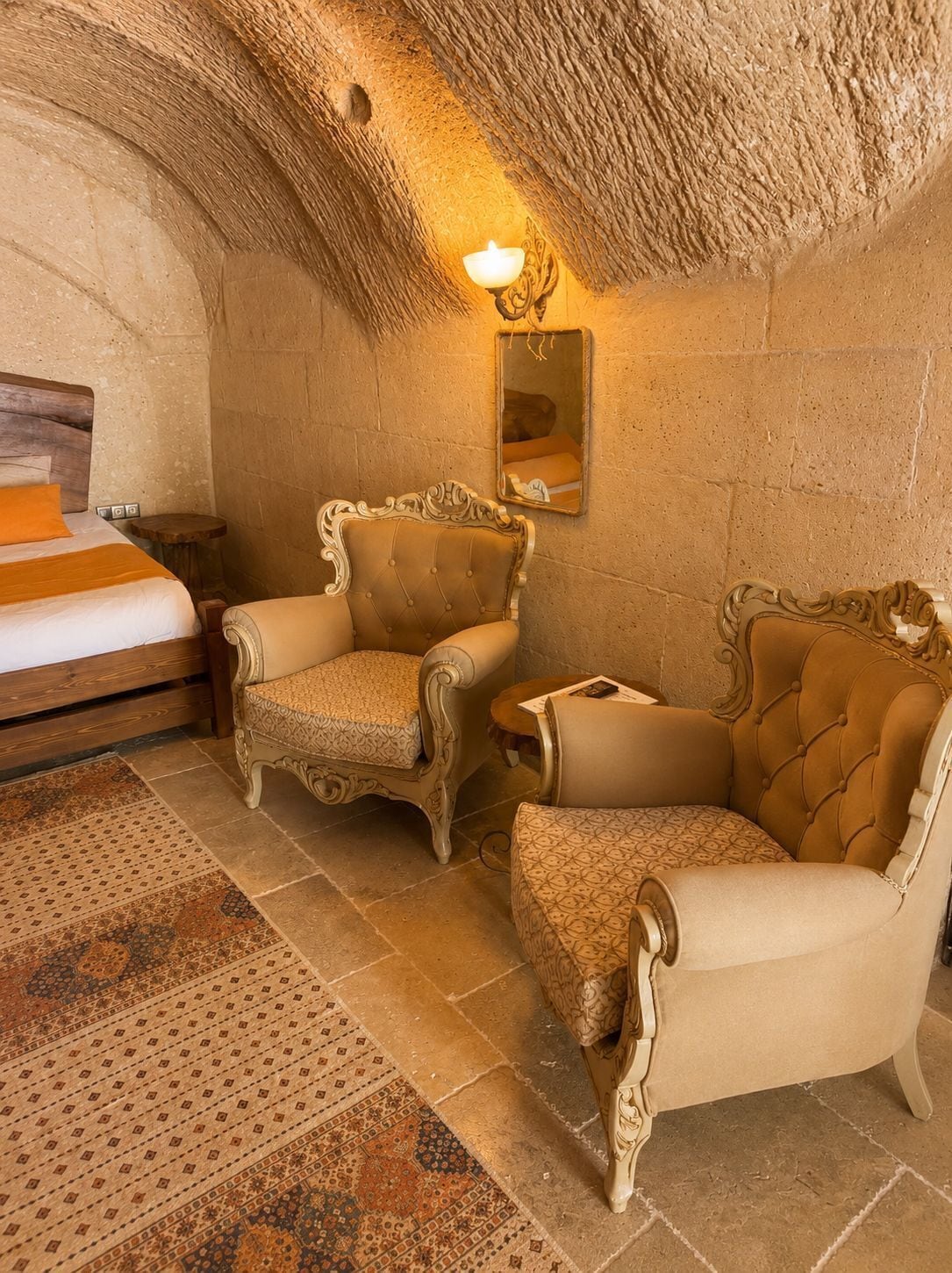 Ein Zimmer mit einem Bett, zwei verzierten Stühlen, einem kleinen Tisch und einem Wandspiegel.