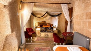 A room with a bed, a table, two chairs, a rug, and pottery on the floor. - Cappadocia Cave House (Ürgüp)