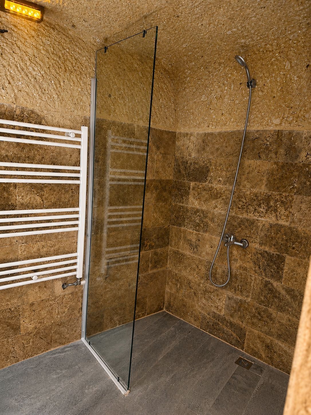 Une douche fermée par des parois de verre, dotée d’un pommeau de douche à main, d’un porte-serviettes blanc et d’un mur à texture.
