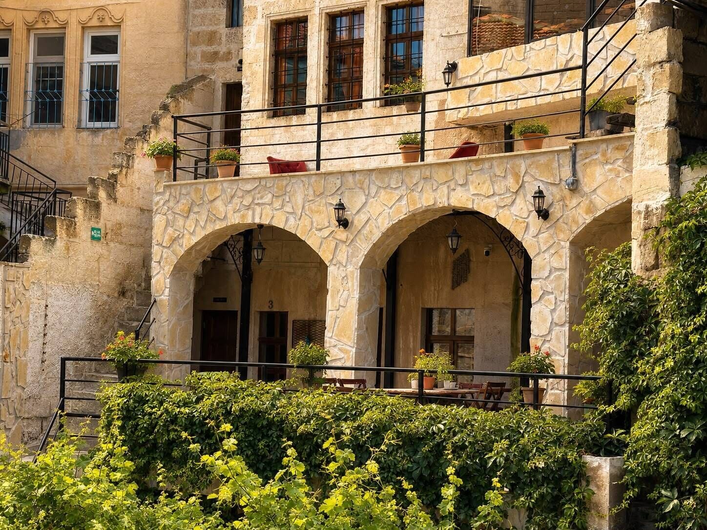 A stone building with a balcony, arched doorways, and potted plants.