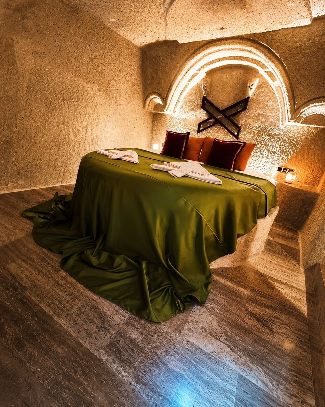 A room with a bed, pillows, a table, and a wall-mounted light fixture.