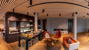 Un interior moderno con techo de madera curvada, una zona de bar central con diversos alimentos y bebidas, y un rincón de estar acogedor con chimenea.