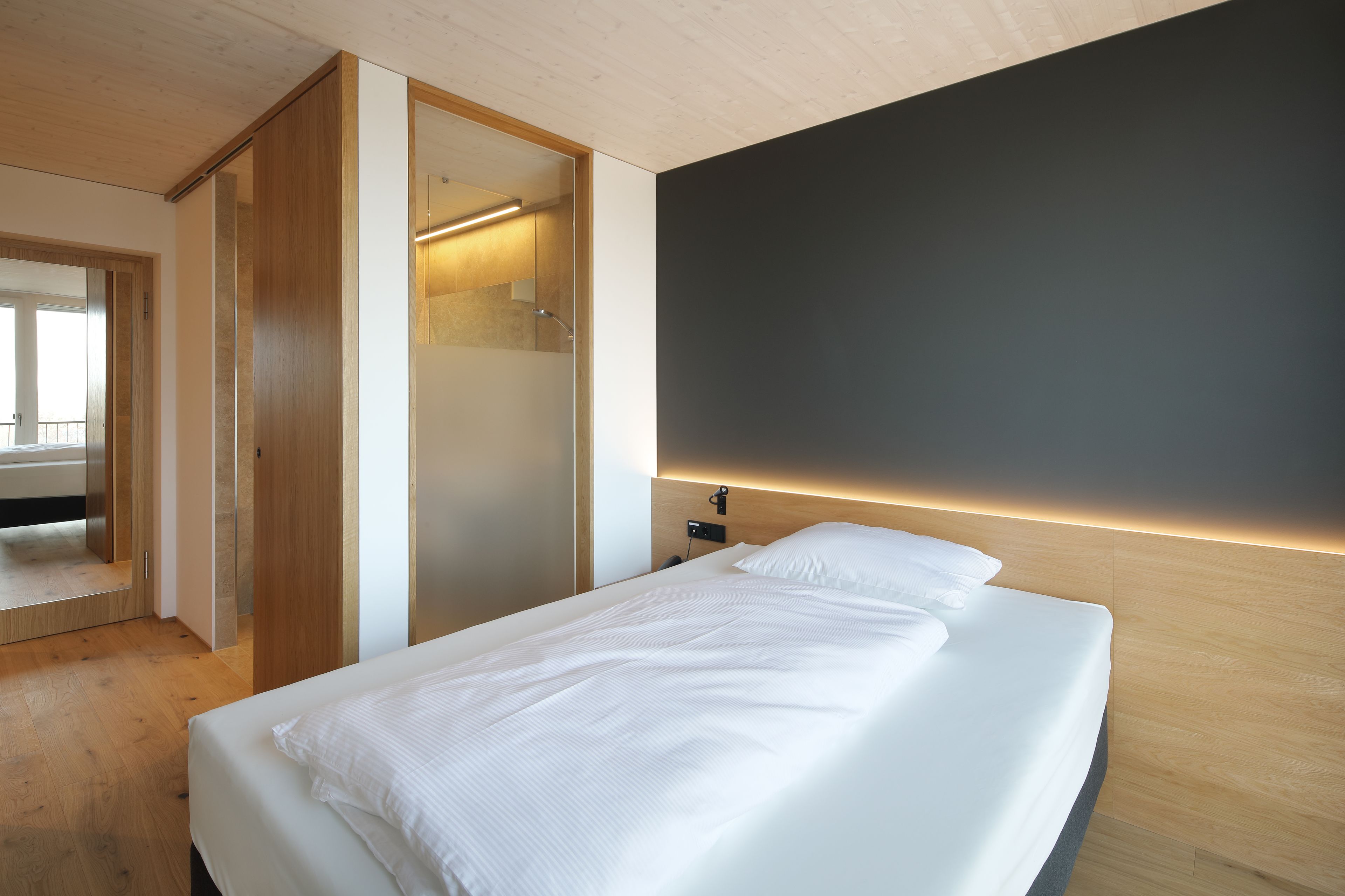 A modern bedroom with a bed, wooden wardrobe, and a dark accent wall.