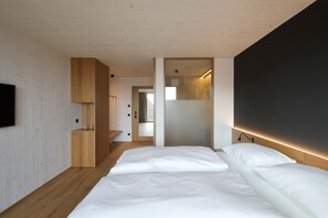 A modern bedroom with a wooden floor, a bed with white bedding, a TV on the left, and a dark accent wall. - 2nd Home Hotel (Nördlingen)