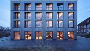 Un edificio moderno de varios pisos con amplios ventanales y balcones, que cuenta con un espacio central abierto con asientos.