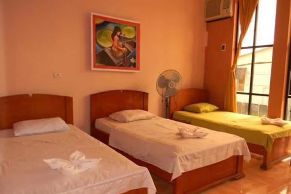 A hotel room with two beds, a fan, a window with curtains, and a painting on the wall.