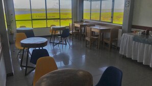 A dining area with tables and chairs, large windows with a view of a green field, and a sign on the wall. - Amazon Dream Hostel (Iquitos)