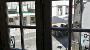 A view through a window with a metal gate, a street with buildings, and outdoor seating. - Casa da Travessa (Ponte de Lima)