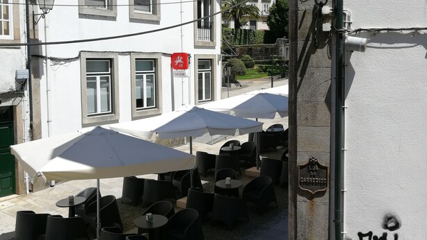 A street view with outdoor seating, a white building with a red sign, and a metal pole with graffiti. - Casa da Travessa (Ponte de Lima)