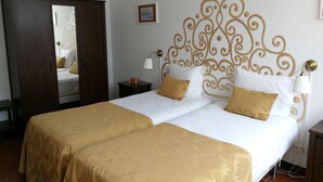 A double bed with a gold and white bedspread, a wooden wardrobe, a nightstand with a lamp, and a decorative headboard. - Casa da Travessa (Ponte de Lima)