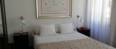 A neatly arranged bedroom with a bed, two bedside tables, a framed artwork, and a window with curtains.
