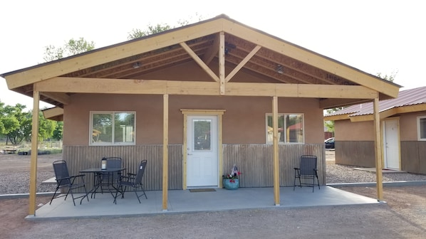 A covered outdoor seating area with a table and chairs, a door, and windows.