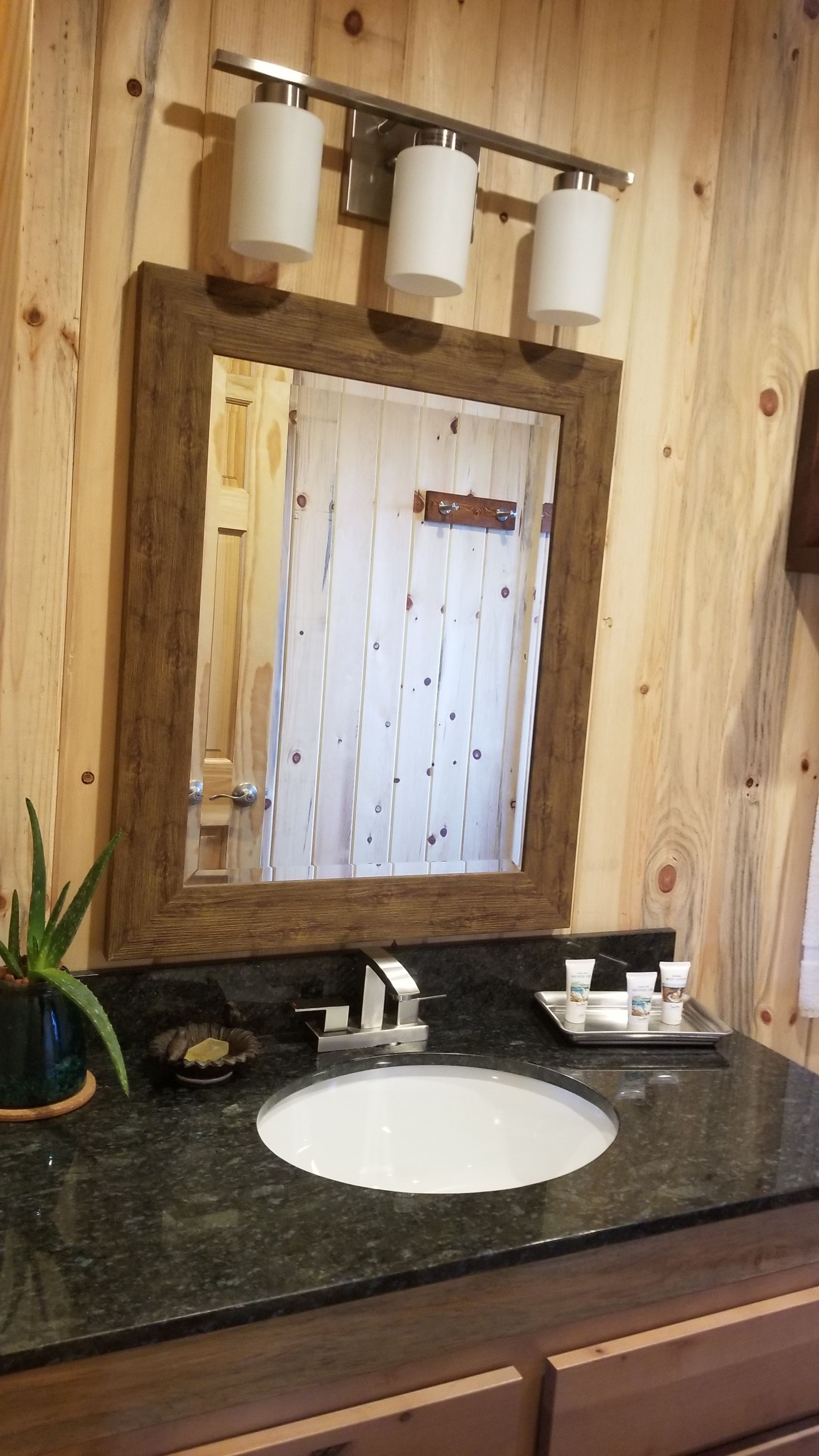 Une salle de bain avec un mur en bois, un grand miroir, un lavabo blanc et un plan de toilette avec des articles de toilette.