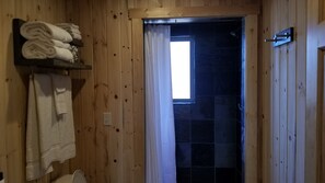 A wooden bathroom with a shower area, a towel rack with folded towels, and a window allowing natural light. - Bluff Gardens Cabins (Bluff)