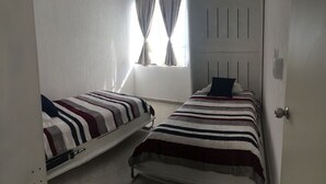 A small, single-room accommodation with two single beds, a window with curtains, and a door. - Olivos Apart (Playa del Carmen)