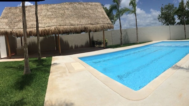 A swimming pool with a thatched roof structure, surrounded by a concrete deck and palm trees. - Olivos Apart (Playa del Carmen)