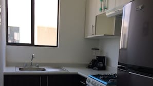 A compact kitchen with a gas stove, oven, and a refrigerator. A window provides natural light, and there are cabinets above the counter. - Olivos Apart (Playa del Carmen)