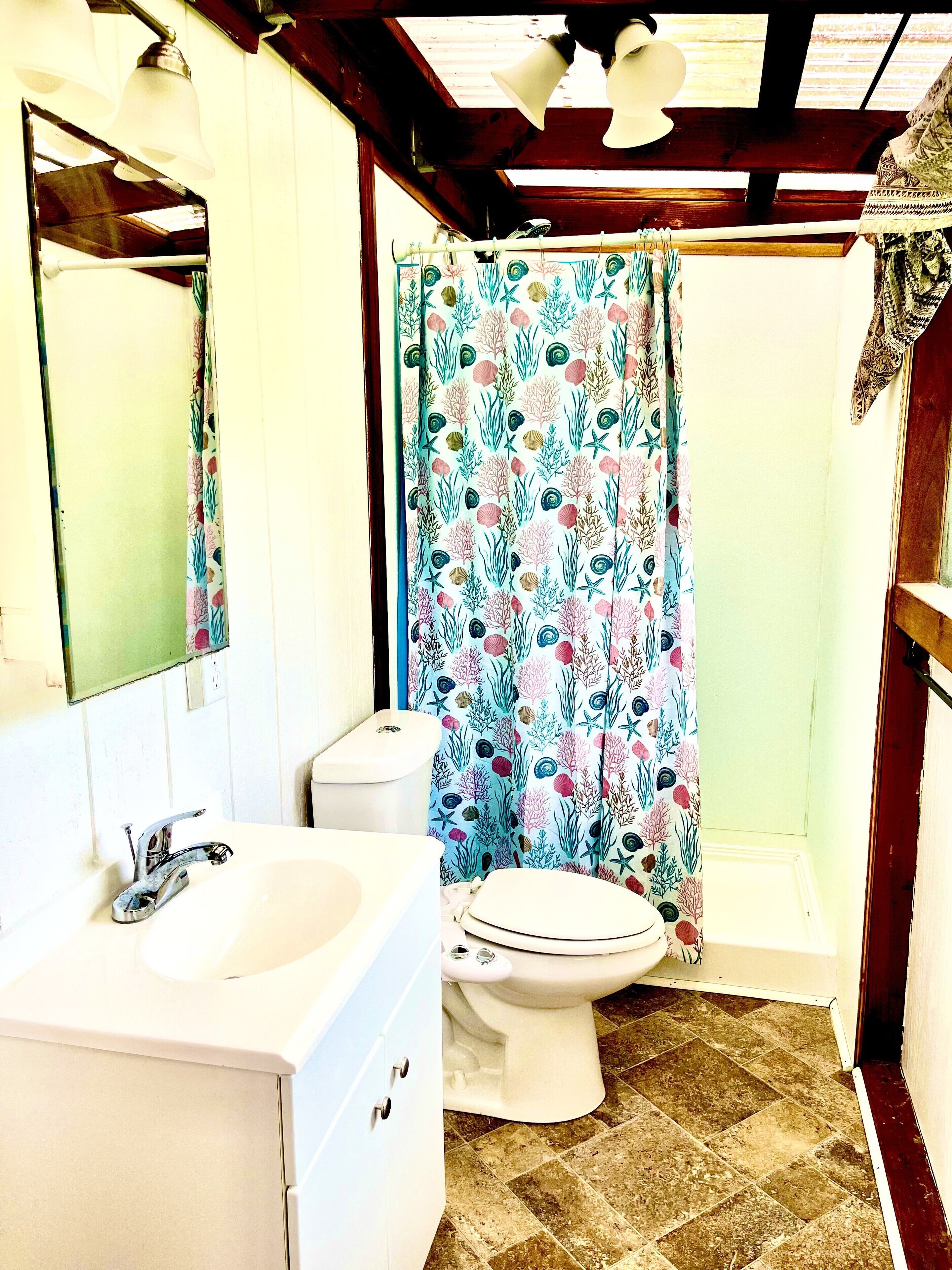 Une salle de bain avec un lavabo blanc, des toilettes et un rideau de douche à motifs floraux.