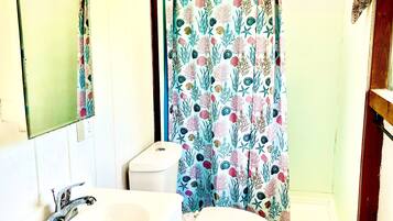 Une salle de bain avec un lavabo blanc, des toilettes et un rideau de douche à motifs floraux.