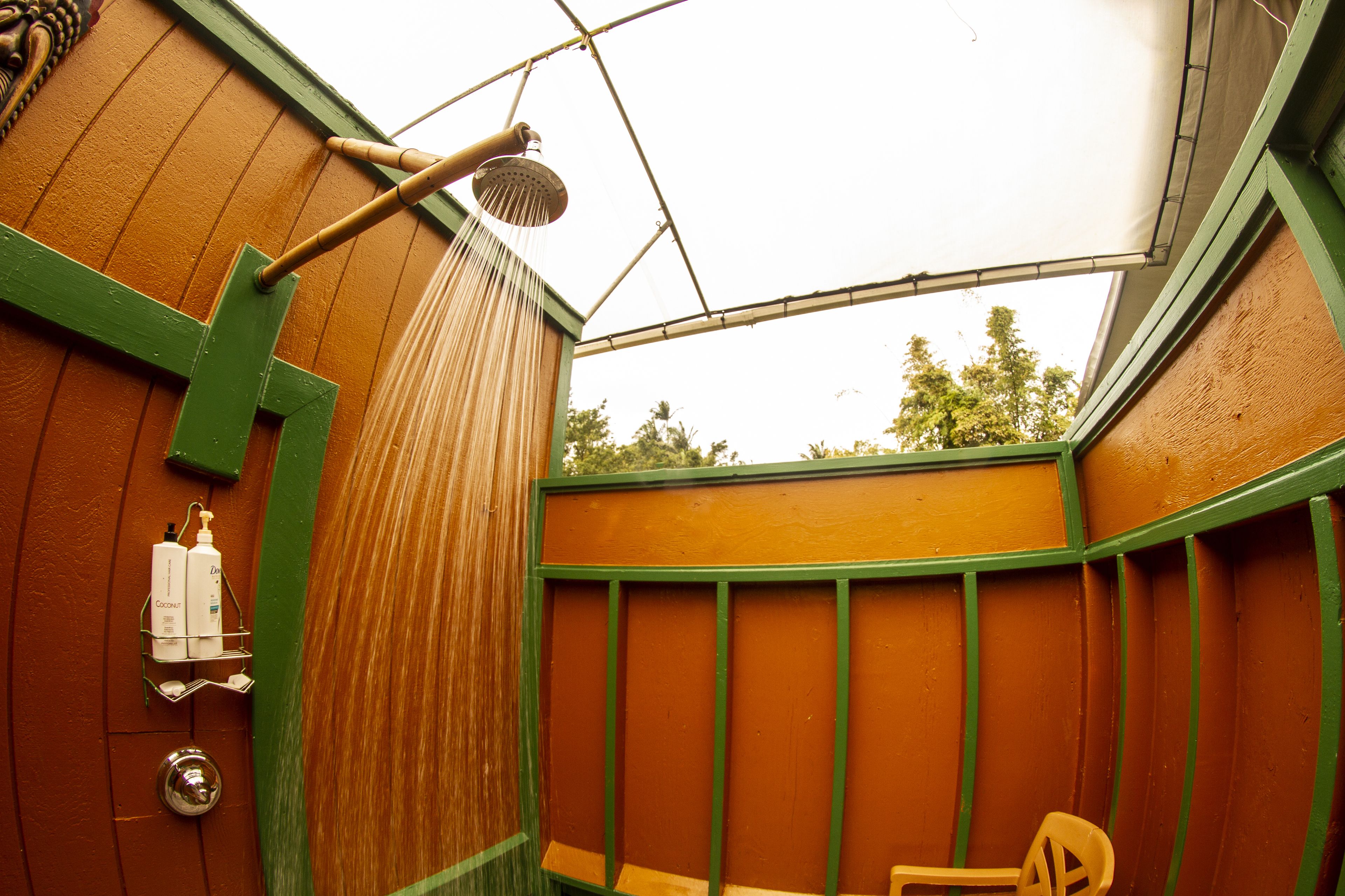 Un baño de madera con ducha, una ventana con marco verde y un perchero con botellas.