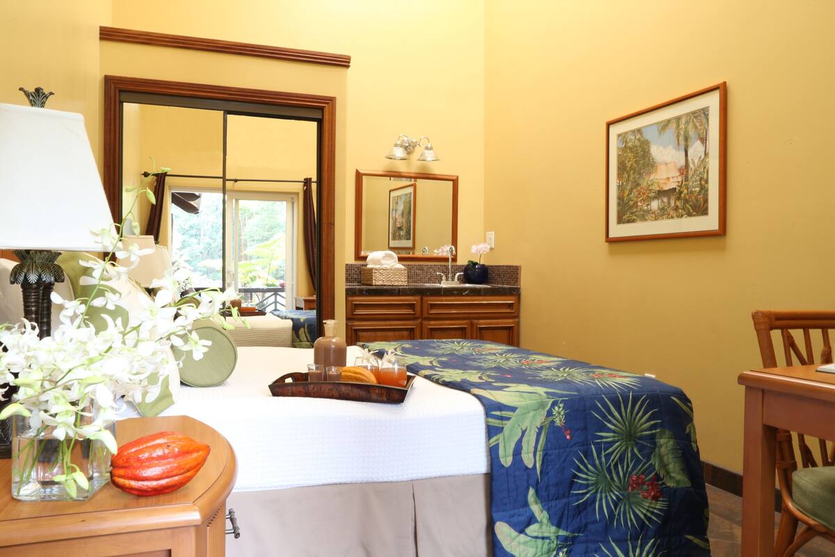 A hotel room with a bed, a desk with a lamp, a chair, a dresser, a mirror, and a painting on the wall.