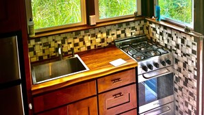 A kitchen with a large window, a hanging light fixture, a stove, and a refrigerator. - Hawaiian Sanctuary (Pahoa)