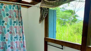 Un baño con un lavamanos blanco, un inodoro y una cortina de ducha con motivos marinos. Se ve una ventana con vistas a la vegetación.
