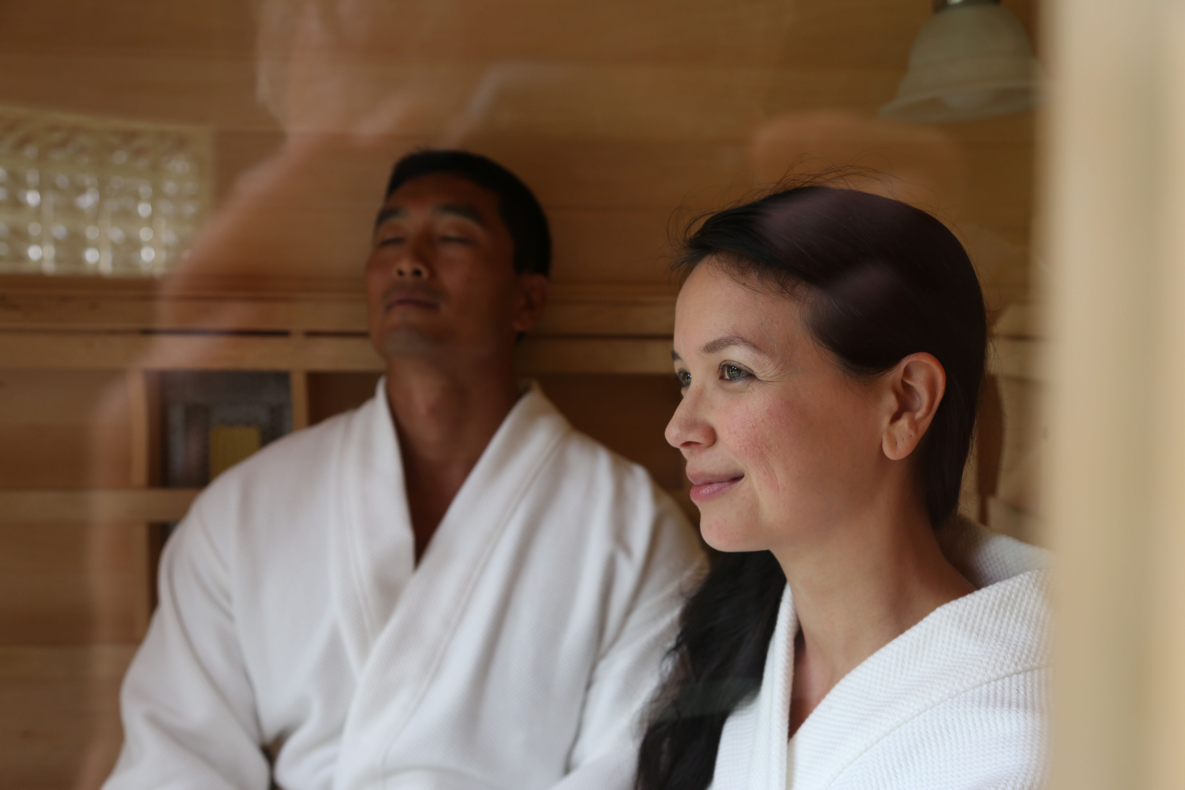 A wooden interior with two individuals in white robes, suggesting a spa or sauna setting.