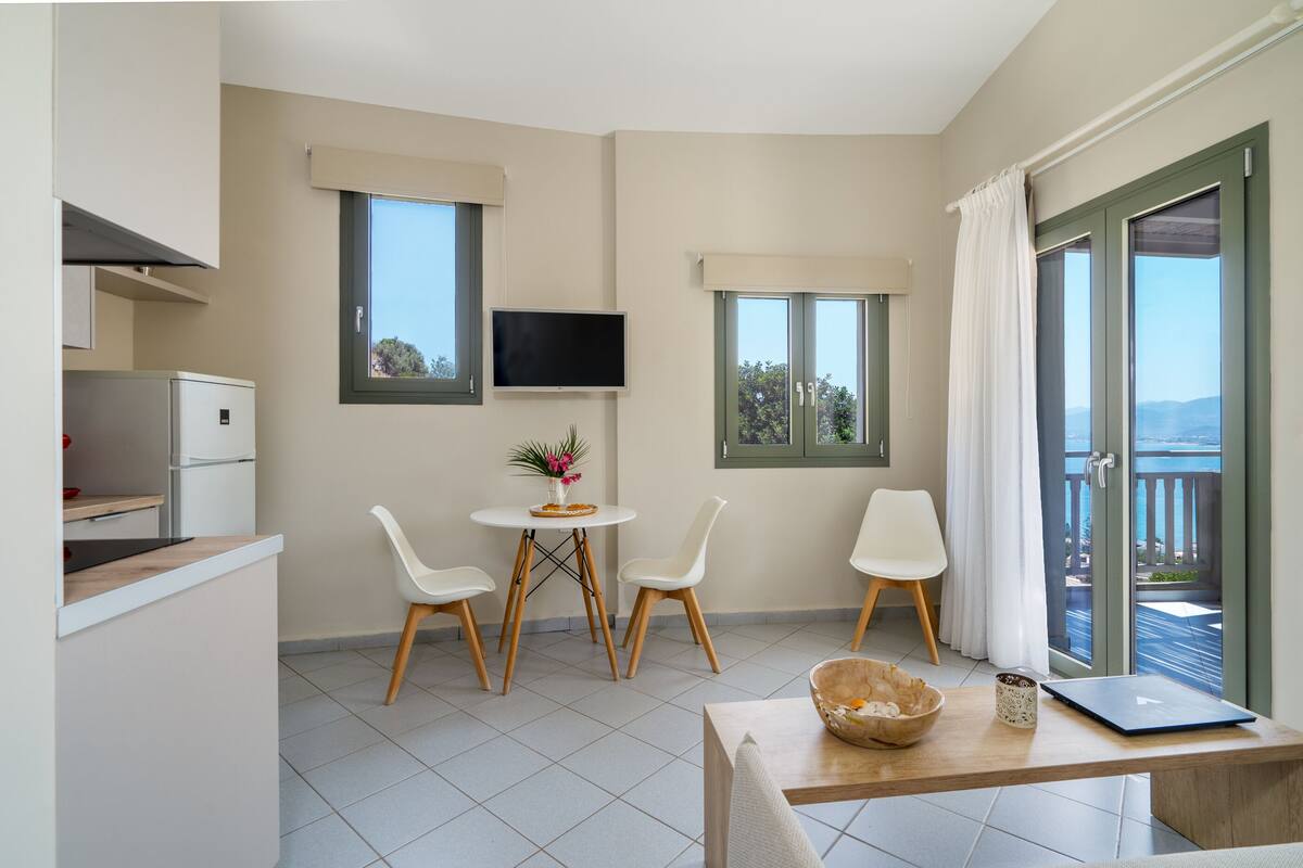 Una cocina moderna con refrigerador integrado, un comedor con mesa y sillas, un televisor de pantalla plana montado en la pared y un balcón con vistas.