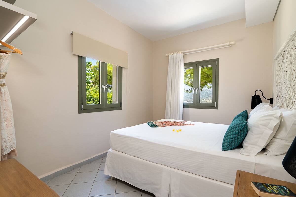 Un dormitorio con una cama, dos ventanas, una cortina, una mesa de madera y una silla.