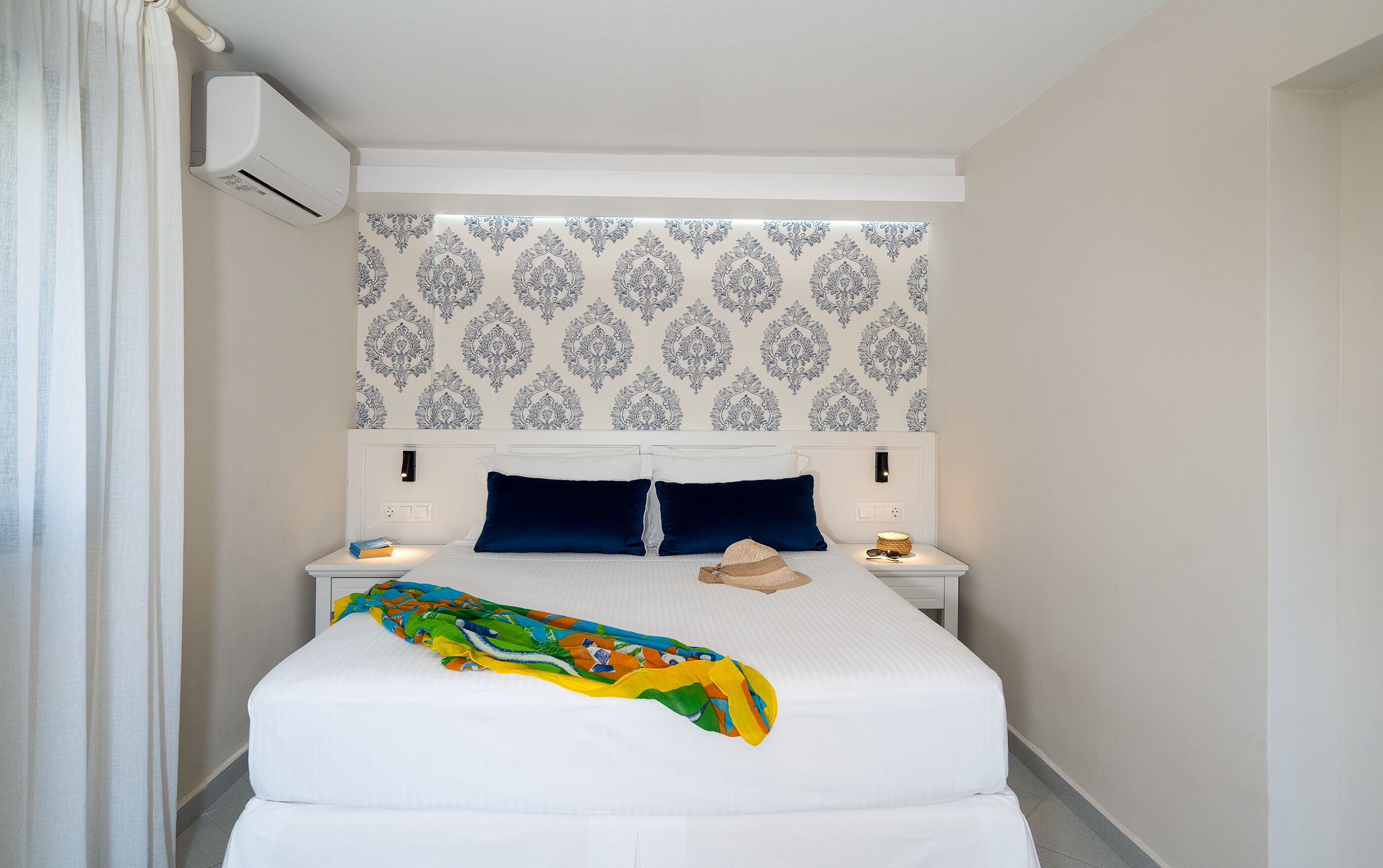 Una cama bien hecha con un edredón de colores, un cabecero de papel tapiz estampado y lámparas de noche.