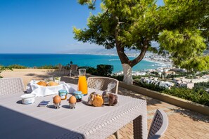 A breakfast table with food and drinks, overlooking a coastal view with a tree and buildings. - Blue View Villas (Hersonissos)