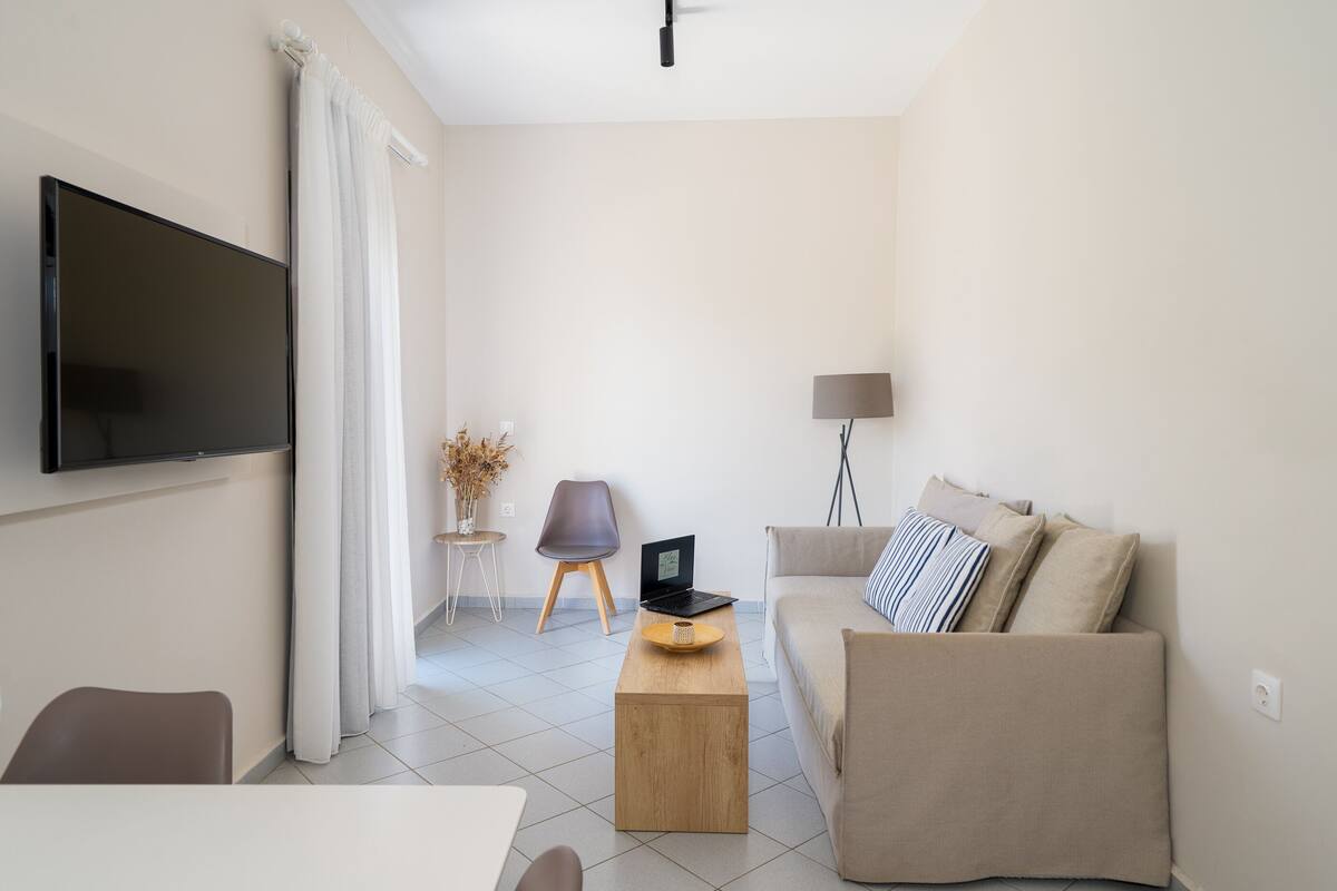 Una sala de estar moderna con un televisor de pantalla plana, un sofá, una mesa de centro y una computadora portátil sobre una mesita auxiliar.