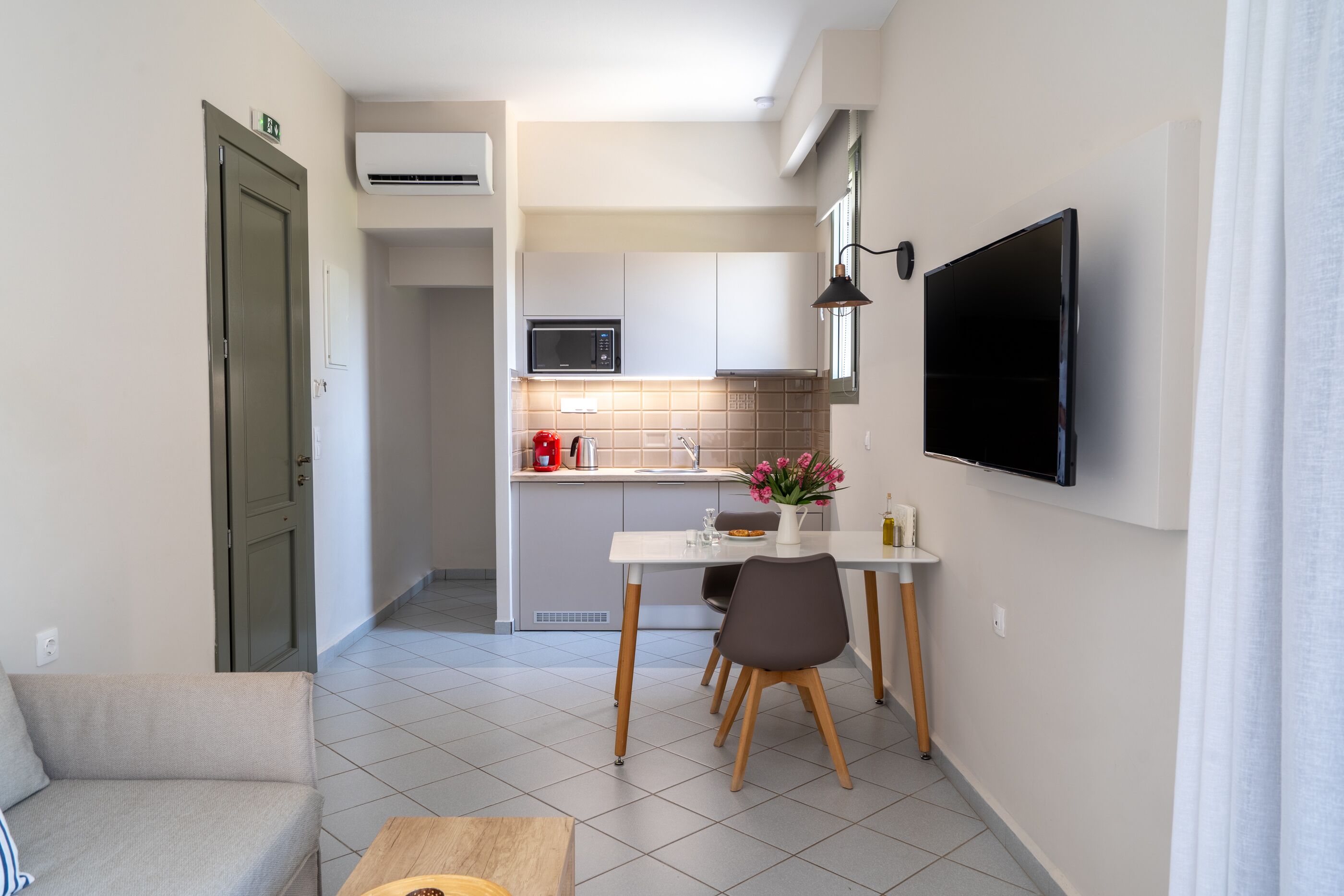 A compact kitchen with a microwave, a dining table with chairs, and a TV mounted on the wall.