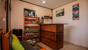 Una zona de recepció amb un taulell de fusta, un sofà amb coixins, una prestatgeria amb revistes i una paret amb cartells.