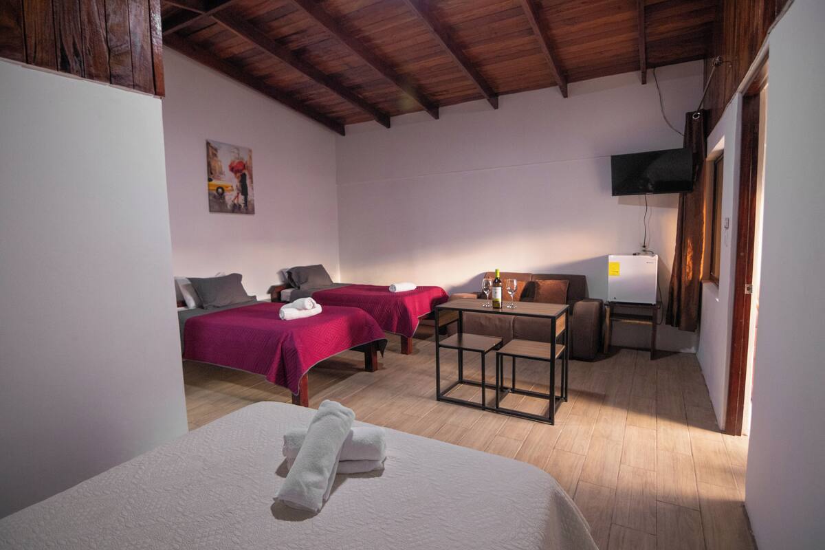 A hotel room with two beds, a small table, a TV, and a wooden ceiling.