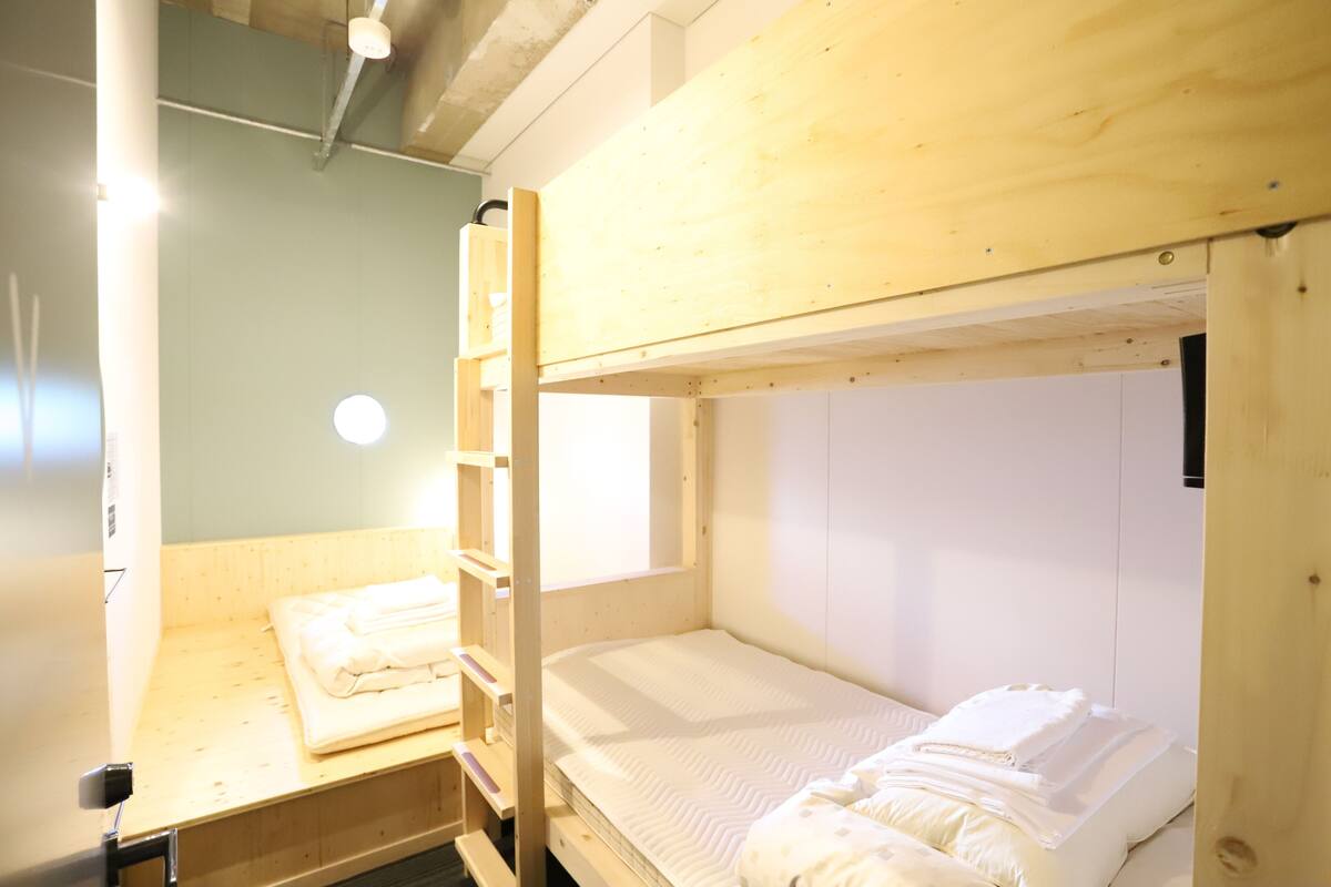A bunk bed room with a wooden bunk bed, a small desk, and a window.